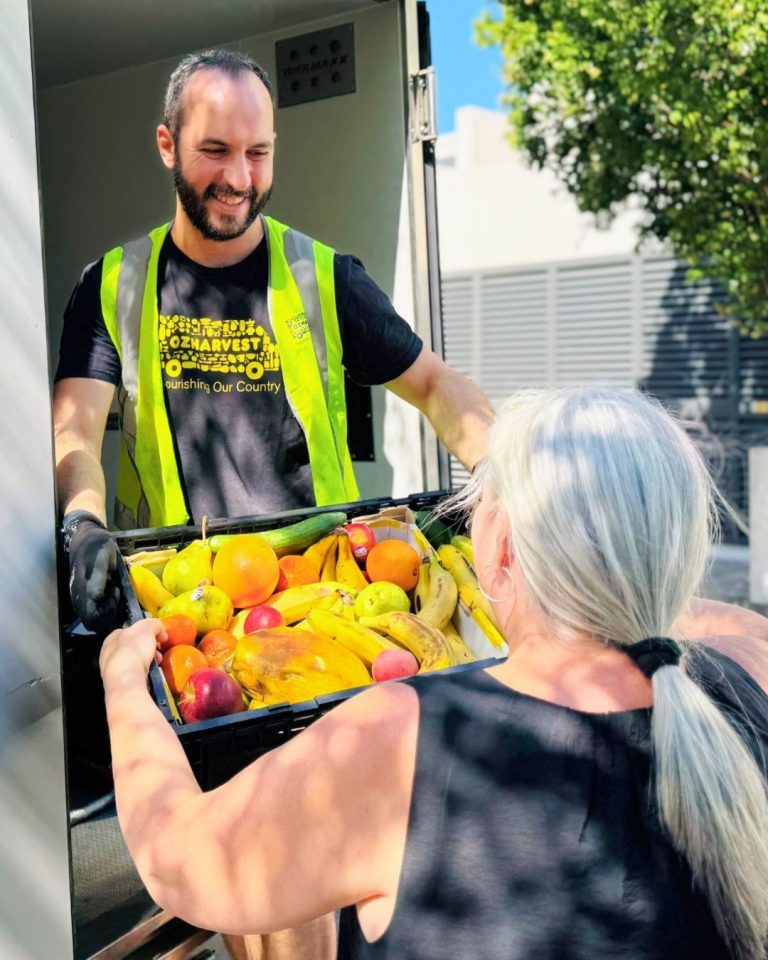 OzHarvest volunteer in hi-vis vest handing a crate of rescued fruit from a delivery van