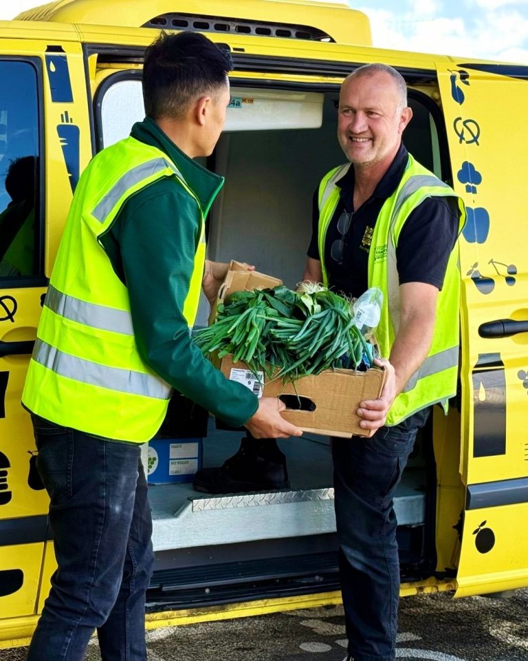 Two volunteers in hi-vis vests loading a box of rescued greens into a yellow OzHarvest van