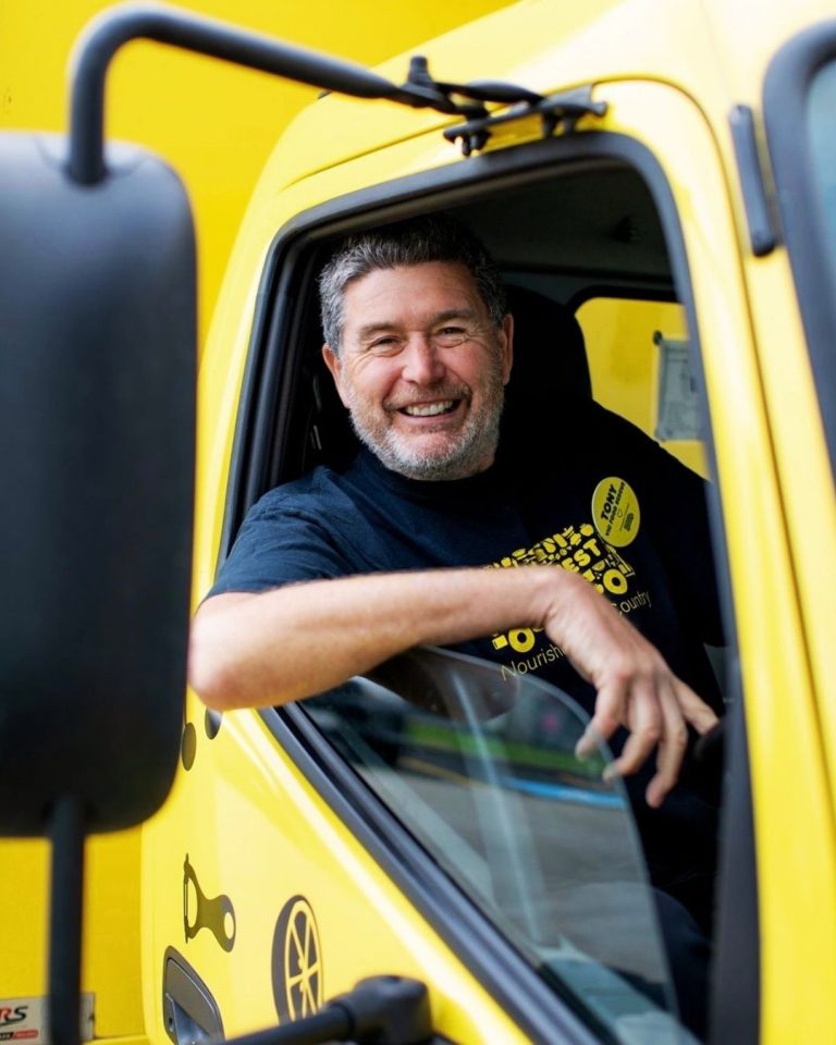 Smiling bearded OzHarvest driver leaning from the window of a bright yellow rescue truck