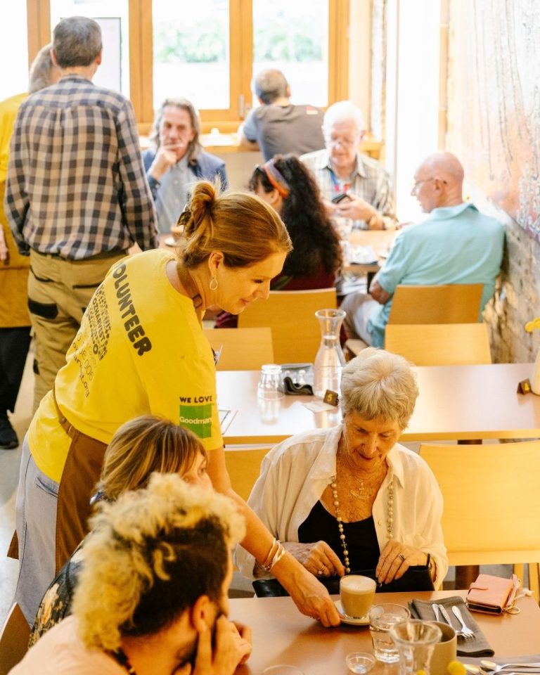 OzHarvest volunteer in yellow shirt serves coffee to seated diners in a busy Refettorio restaurant