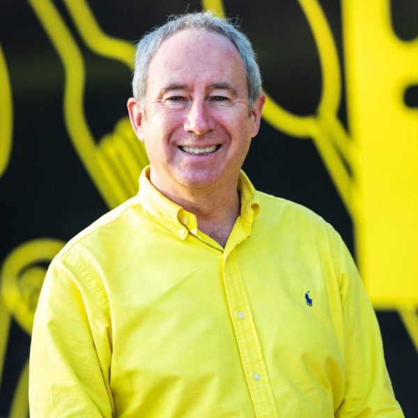 Smiling man in a yellow shirt standing in front of a black and yellow OzHarvest van graphic